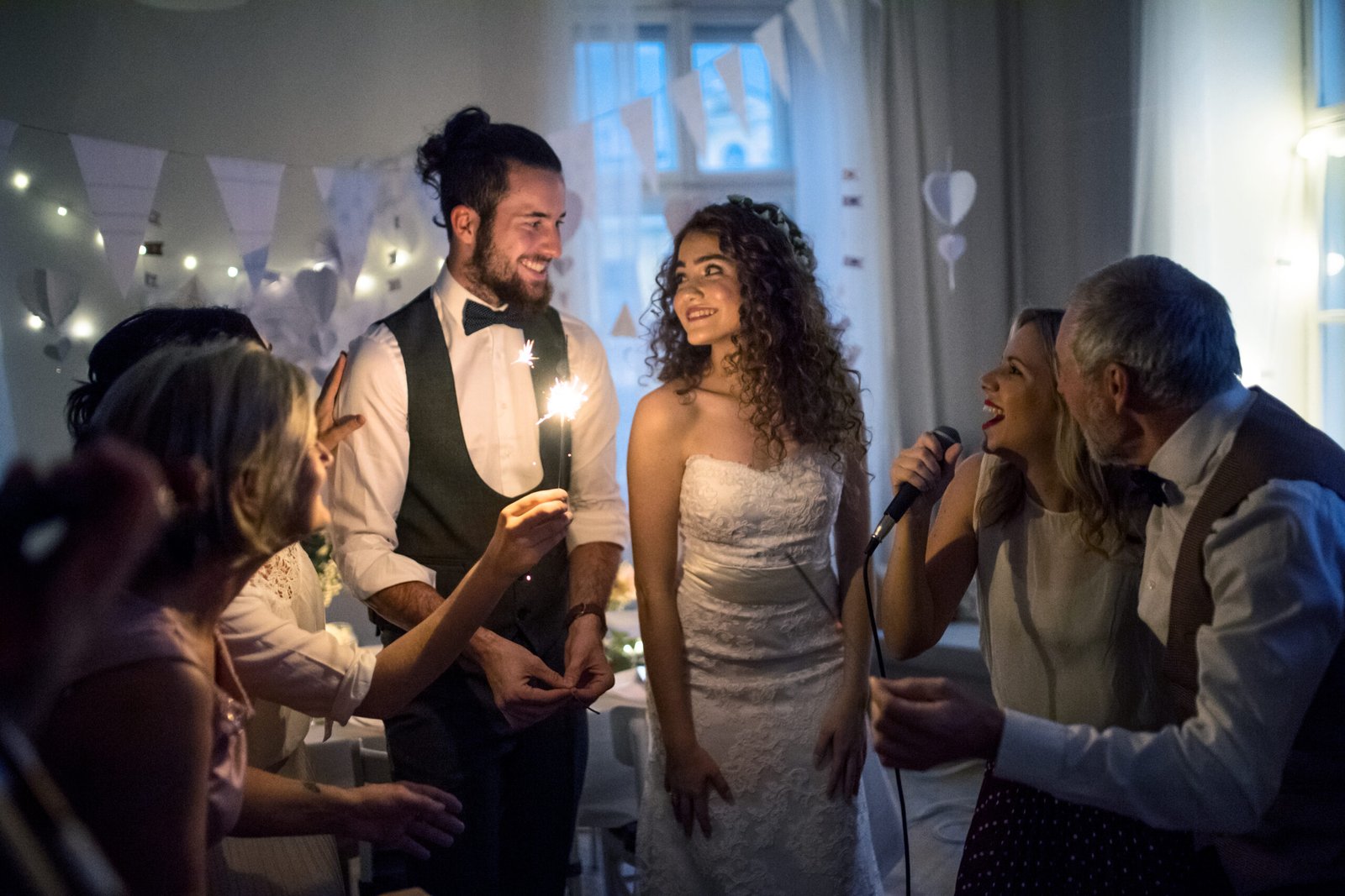 A young bride and groom with other guests dancing and singing on a wedding reception.